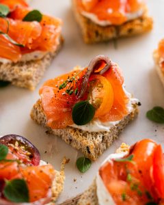 Bite-sized toast appetizers with homemade gravlax, tomato slices, and fresh herbs
