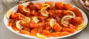 Thinly sliced healthy cured salmon (gravlax) arranged on a serving platter with lemon zest
