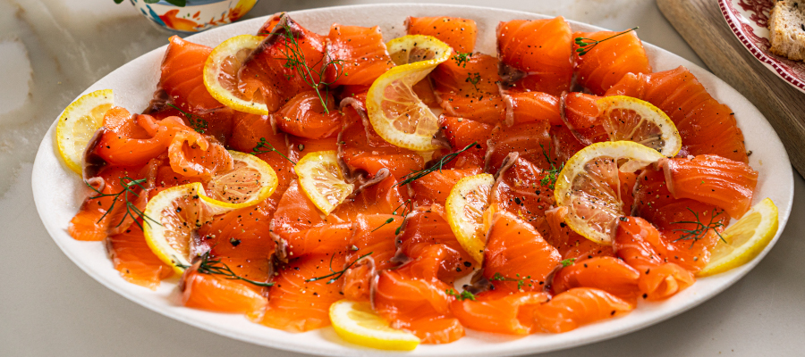 Thinly sliced healthy cured salmon (gravlax) arranged on a serving platter with lemon zest