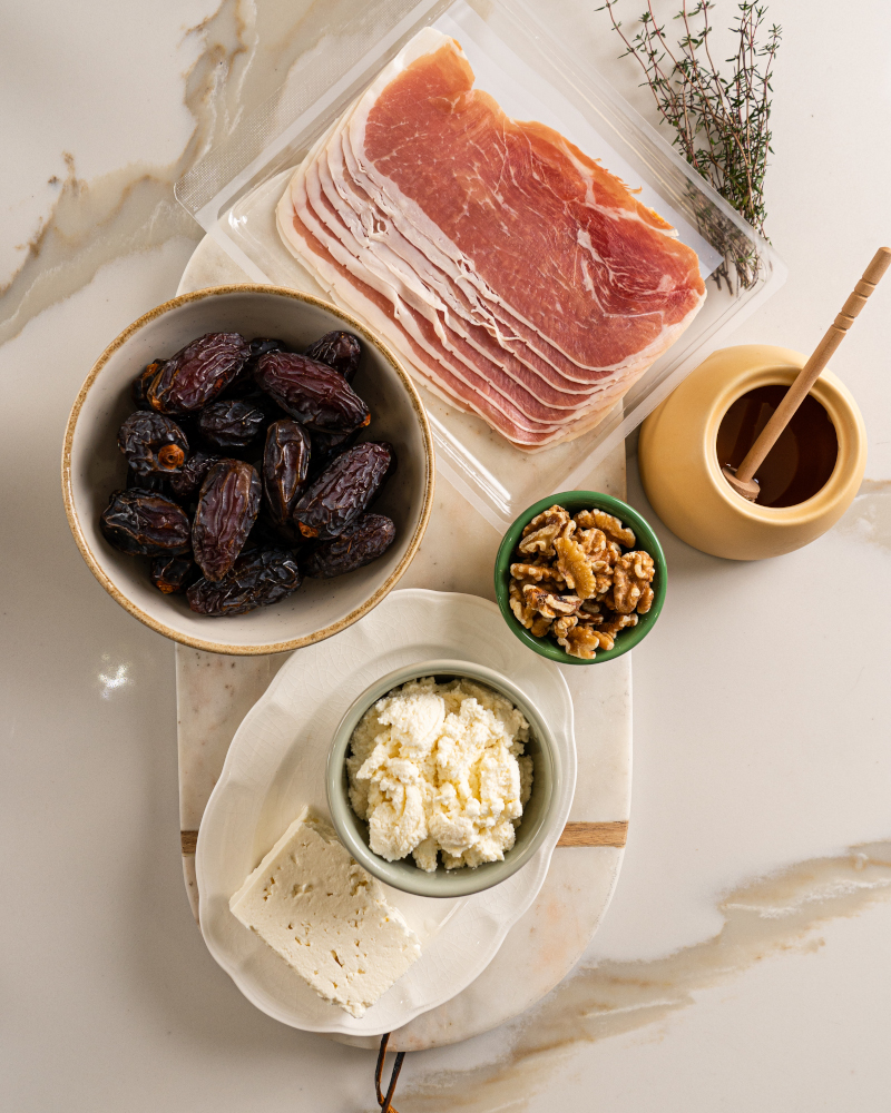 Ingredients for healthy cheese stuffed dates including Medjool dates, light ricotta, feta cheese, walnuts, prosciutto, and honey