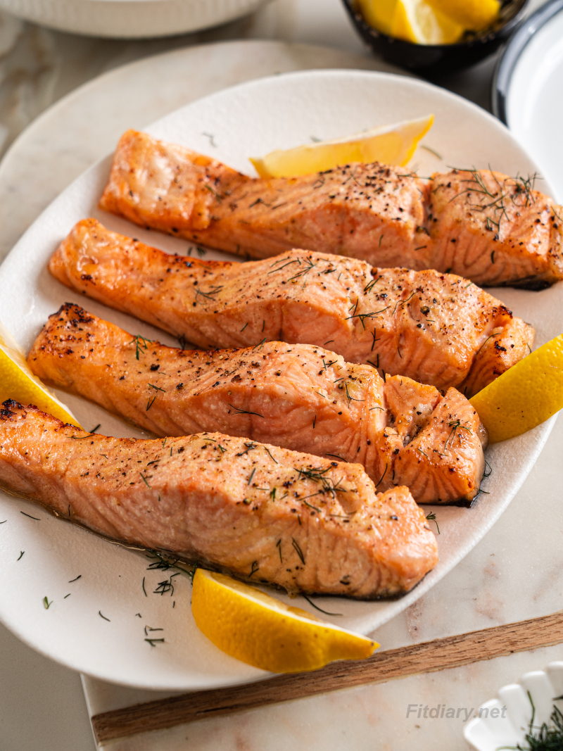 Juicy air fryer salmon served on a plate with fresh lemon wedges and herbs
