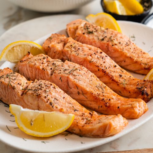 Juicy air fryer salmon served on a plate with fresh lemon wedges and herbs