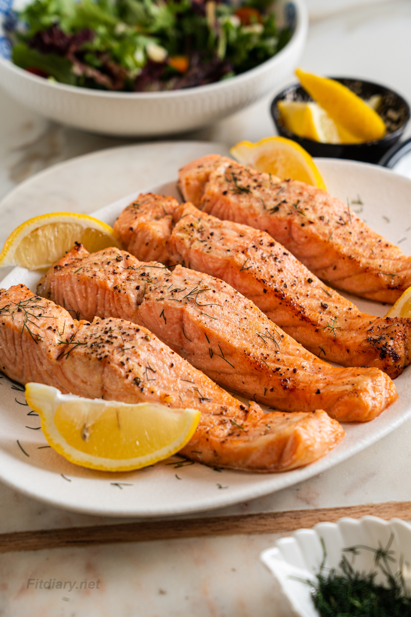 Juicy air fryer salmon served on a plate with fresh lemon wedges and herbs