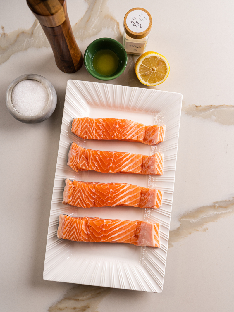 Fresh ingredients for air fryer salmon including salmon fillet, lemon juice, melted butter, garlic powder, salt, and pepper.