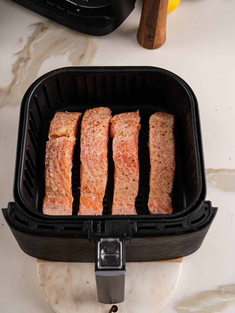 Seasoned salmon pieces placed in air fryer basket ready to cook